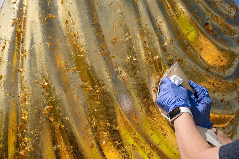 Gold leaf being applied to the statue of Mary atop of the dome during the regilding process.