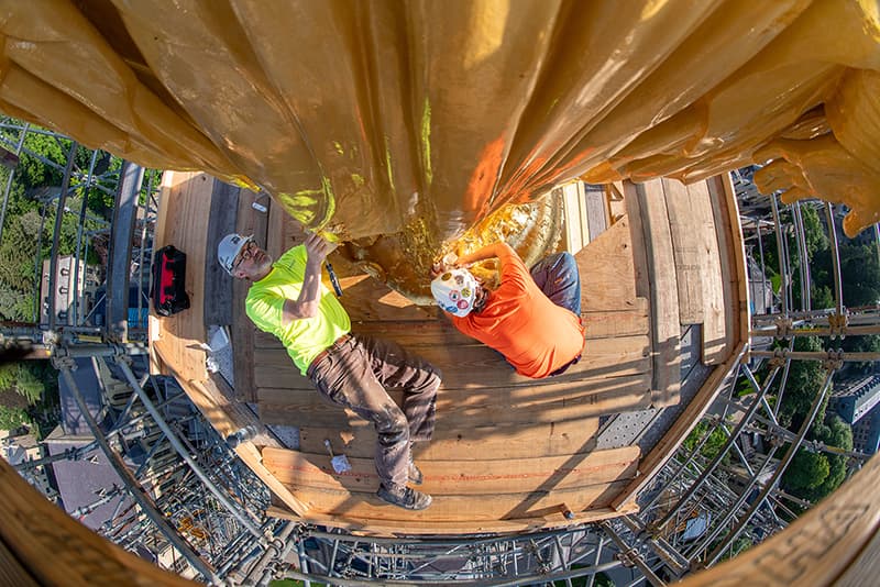 Workers applying gold leaf to the base of the statue of Mary atop the Dome.