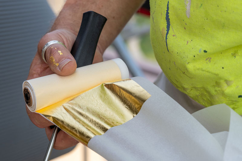 A close up view of a hand holding a roll of paper with gold leaf on it.