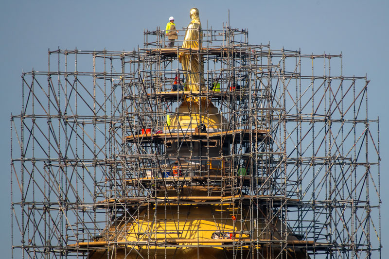 A view of the Golden Dome surrounded by scaffolding. Workers stand and work at various levels of scaffolding.