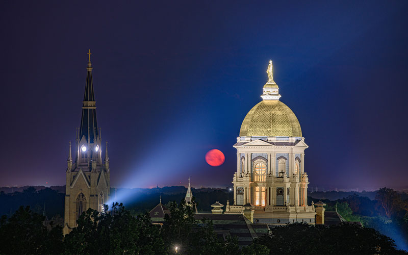 The Golden Dome lit up by a spotlight at night. There's a red moon in the background. 