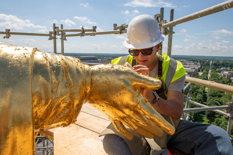 A man puts a layer of thin gold leaf on the statue of Mary on top of the Golden Dome.