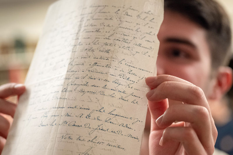 A student holds up a piece of paper with calligraphic writing on both sides of it up to the light.