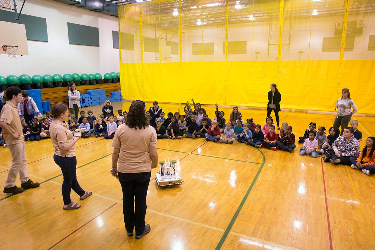 Members of the club doing a demonstrations inside a gymnasium for grade schools students.