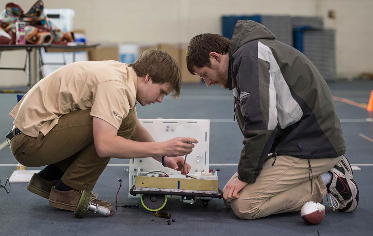 Two College of Engineering students work on a robot.
