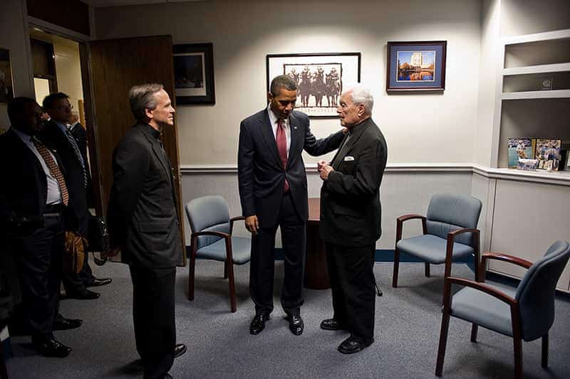 Barack Obama puts his hand on Rev. Theodore M. Hesburgh's shoulder while they have a discussion. Rev. John Jenkins, C.S.C. stands beside them.
