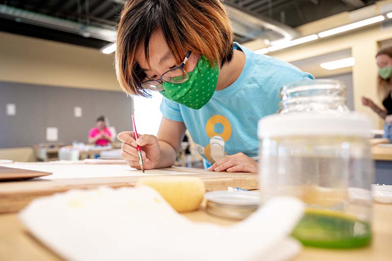 An architecture student wearing a mask does watercolor..