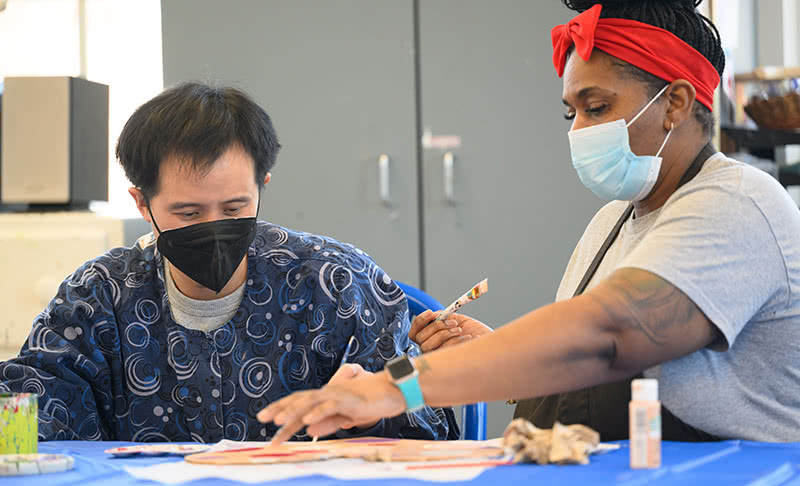 A Misericordia resident and helper are working on a painting at a table.