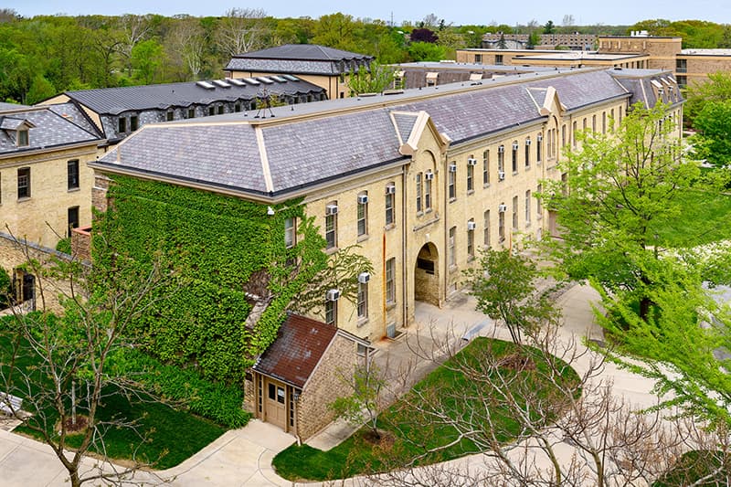 A photo of Brownson Hall. Ivy grows on the south-facing wall. The building is long with two rows of windows. It's visibly aged with rusted bricks and damaged roof tiles.