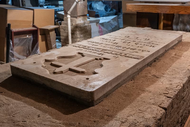 A marble crypt embedded into a concrete slab bears a cross etched on its face.