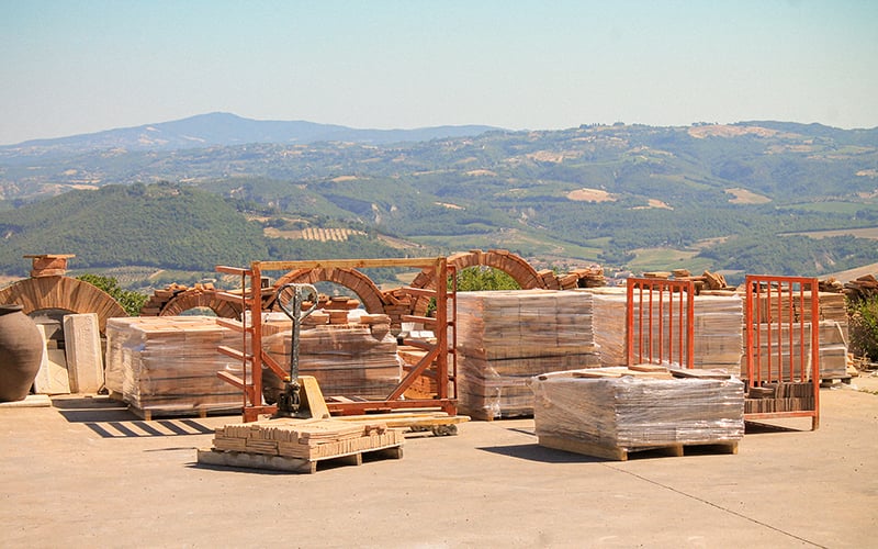 Pallet stacks of bricks in the foreground with the hilly Italian countryside in the background.