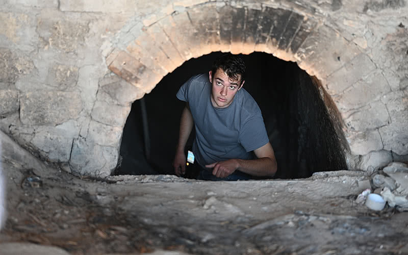 Student working inside the unlit kiln looking out to other workers out of frame.