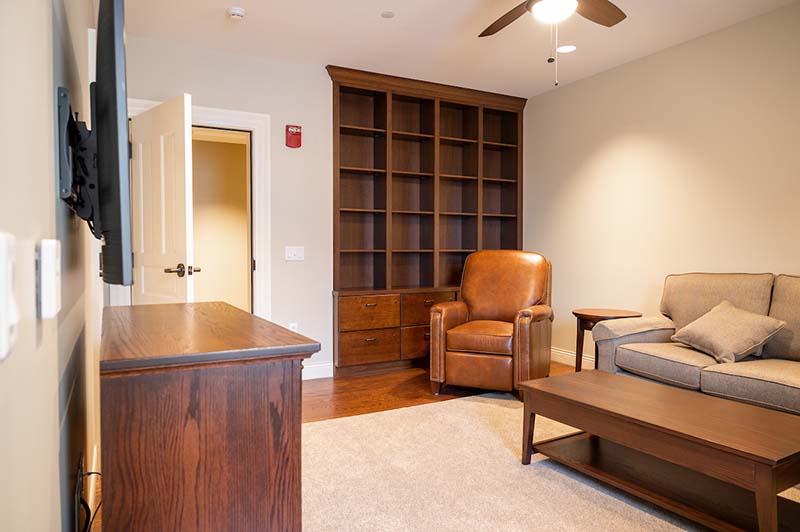 A bedroom with wooden closet, leather chair and tv.