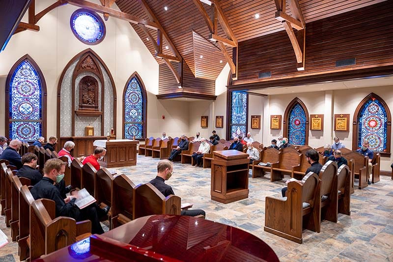 The community sits in prayer in the chapel with blue stained glass.