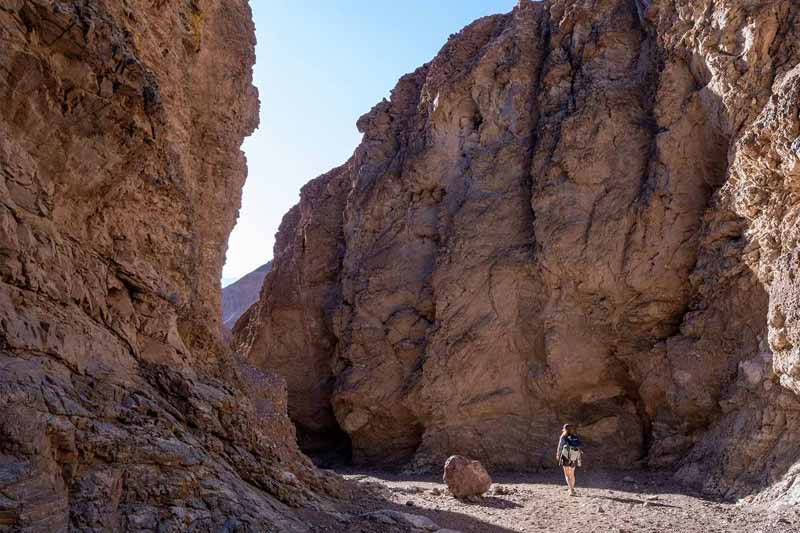 An individual walks between two large rocky moutains.