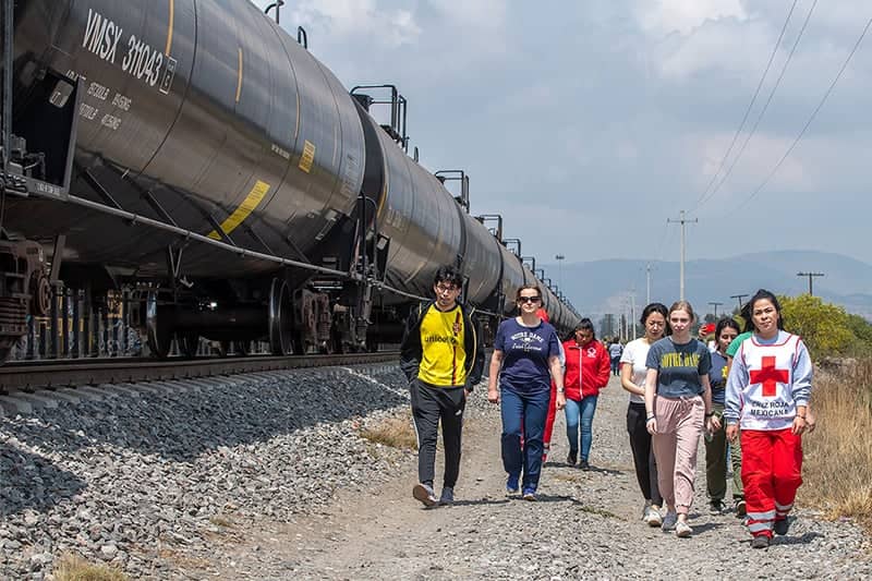 Students walk along a train track with members of the red cross in search of migrants who need assistance