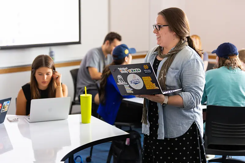 Walden walks around her classroom with laptop in hand surrounded by students.