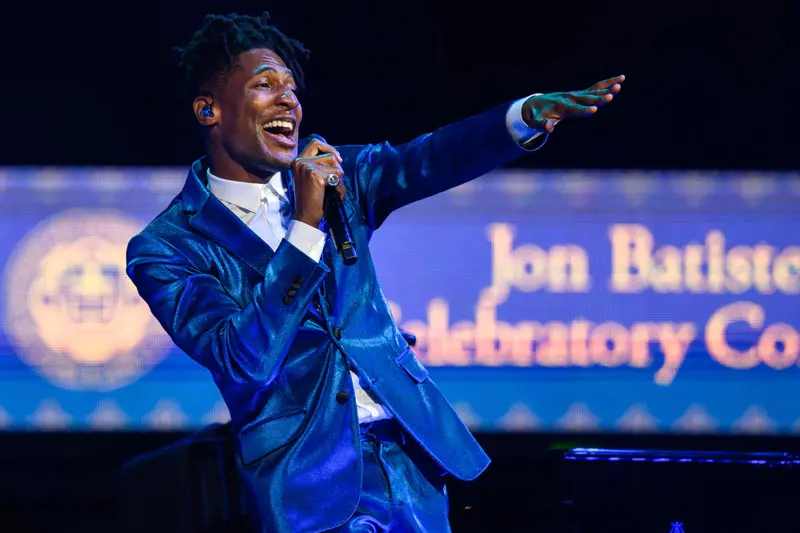 A close up of singer John Batiste with a microphone in his hand.