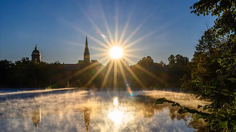 The sun rising over a foggy lake with the Golden Dome and Basilica in the background.
