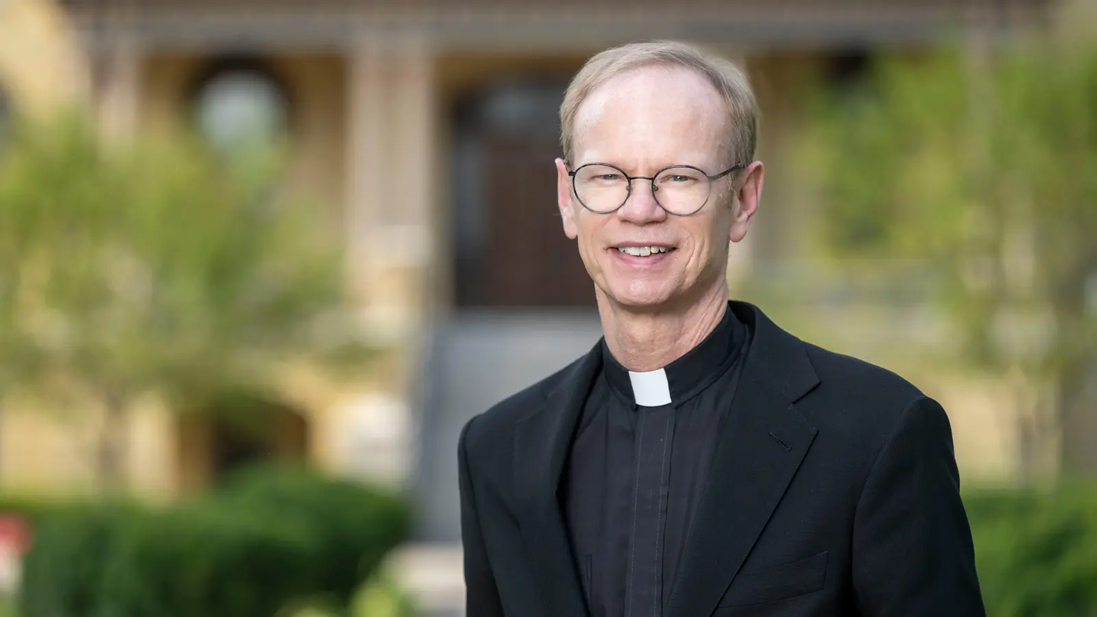 A portait of Fr. Bob Dowd with blurry green landscaping in the background.