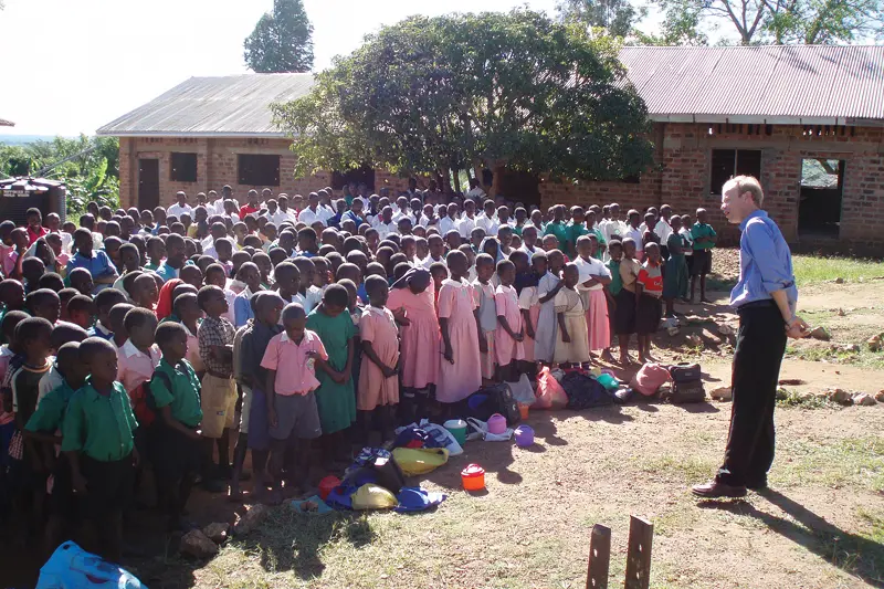 Fr. Bob Dowd stands in front of a large group of black children outside a brick building.