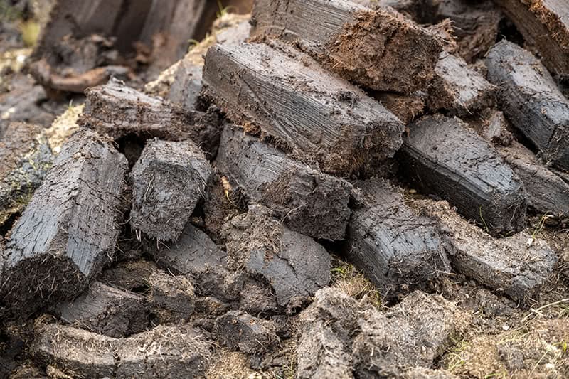 A pile of rectangular slabs of peat freshly removed from the earth.