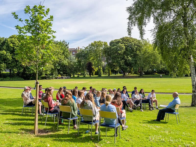 Kevin Whelan speaking to a group of students while sitting in chairs in a park