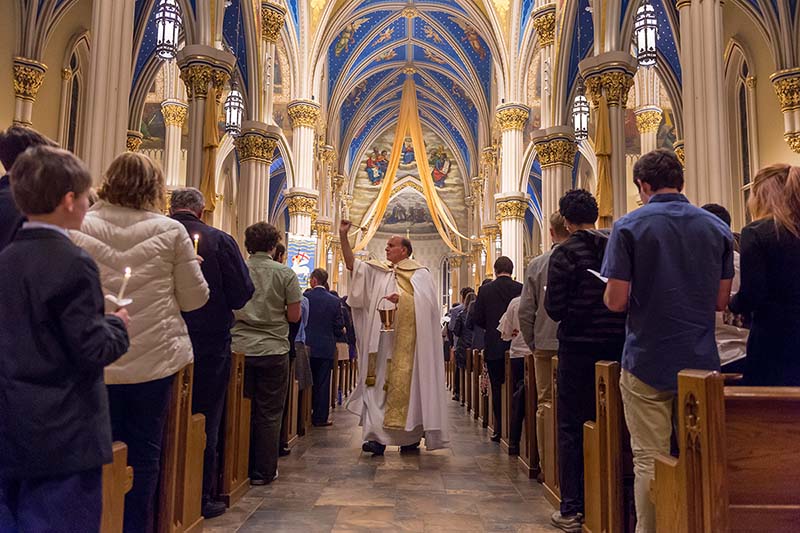 Father Rocca wearing white vestments spreads holy water on the congregation in the Basilica.