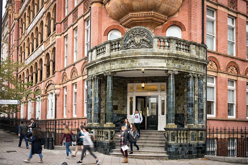 Students come down the stairs of a red brick building.