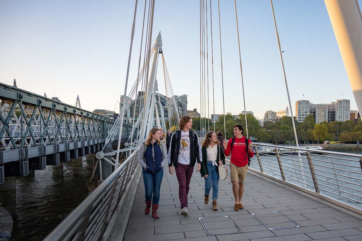 Four students walk on a bridge across the River Thames.