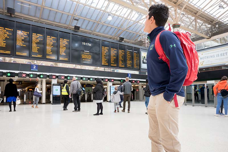 A student with a backpack looks up at the train schedule.