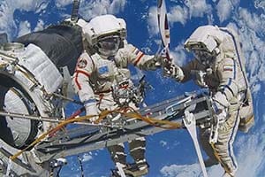 Two astronauts on a space walk with earth behind them.