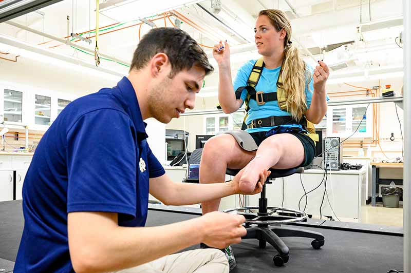 A man attaches sensors to the leg of a woman sitting in a chair talking to someone off camera.