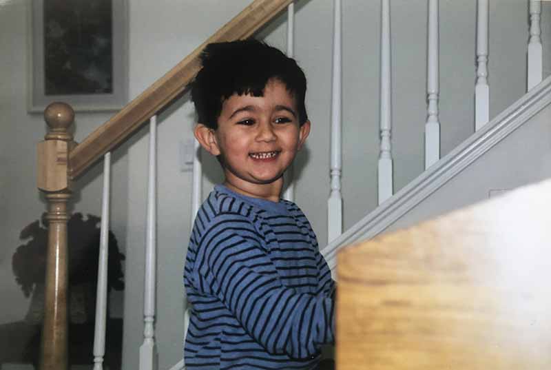 A childhood photo of a young boy smiling and playing the piano.