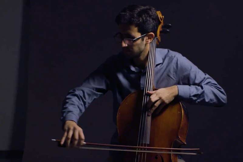 Alex Mansour plays the cello against a dark backdrop.