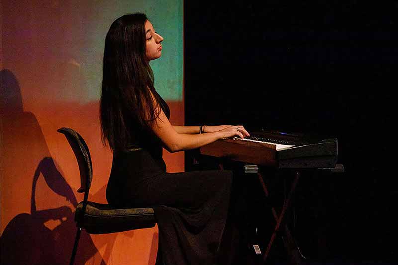 A woman sits at an electric piano and plays with her eyes closed.