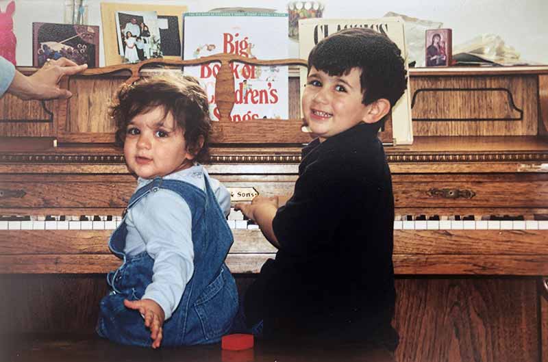A childhood photo of two young children sitting at a piano.