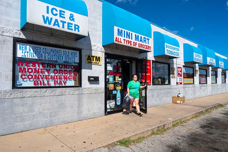 A woman walks outside of a convience store in a strip mall.