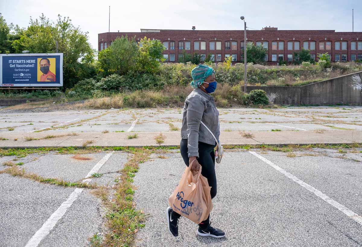 A woman carries grocery bags in both hands walking through an empty parking lot.