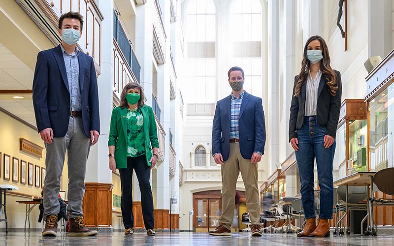 Four people physically distanced and masked pose for a photo in Jordan Hall of Science.
