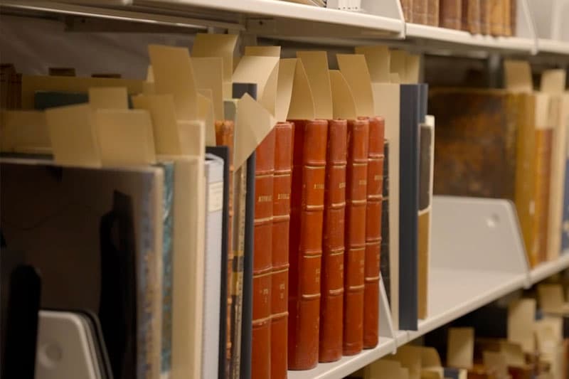 A line of old books on a shelf with slips of paper peeking out from the top.