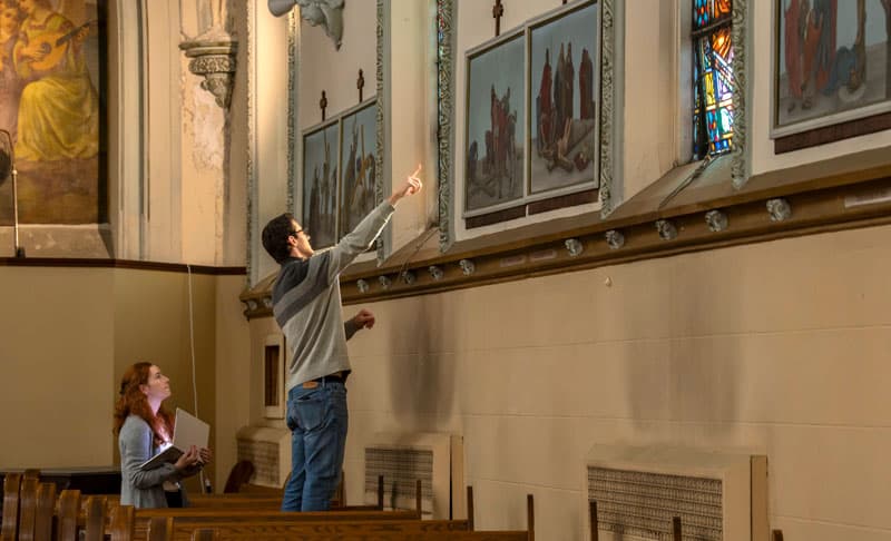 Two students assess and document the damage on the stained glass windows at St. Adalbert Catholic Church in South Bend.