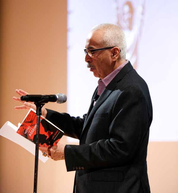 U.S. Poet Laureate Juan Felipe Herrera reading from a red book at a microphone