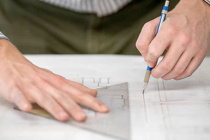 An architectural student drawing using straight edges on a architectural plan of a residential house.