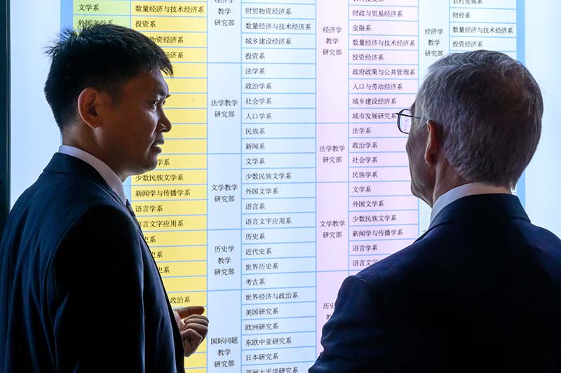 Two men stand in front of a display with Chinese written on it.