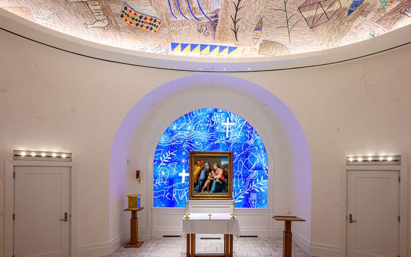 The Queen of Families Chapel in the Raclin Muprhy Museum of Art with a blue stained glass window behind an Italian painting.
