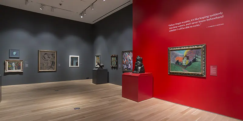 A gallery with paintings and small statues on pedastals against a red wall.