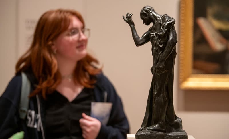 A small bronze statue with a blurred female behind it.