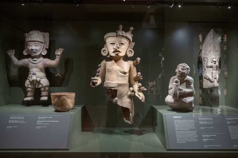 Four gray statues behind a display case.