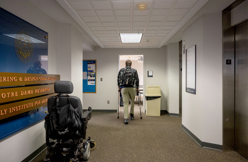 Andrew walks through a door using his crutches. His wheelchair is left behind in the entryway.